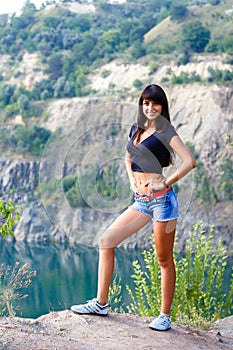 Happy young brunette woman walking on the shore of a mountain ri