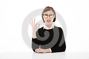 Happy young business lady wearing glasses showing okay gesture.