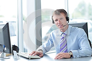 Happy young business man in headset working on computer.