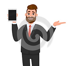 Happy young business man showing/holding blank screen of tablet computer display and presenting/ introducing/pointing something.