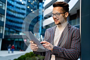 Happy young business man with tablet at work in modern urban background