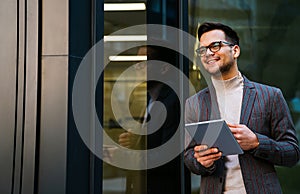 Happy young business man with tablet at work in modern urban background