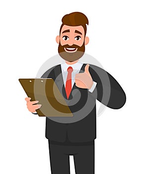 Happy young business man wearing a suit holding clipboard and making or showing thumbs up gesture or sign. Person keeping the file