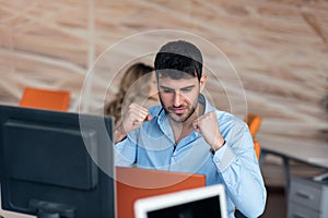 Happy young business man working on desktop computer at his desk in modern bright startup office interior