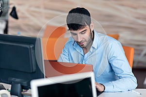 Happy young business man working on desktop computer at his desk in modern bright startup office interior