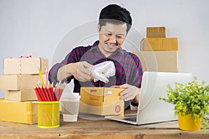 Happy young business owner packing materials and shockproof plastic into cardboard boxes