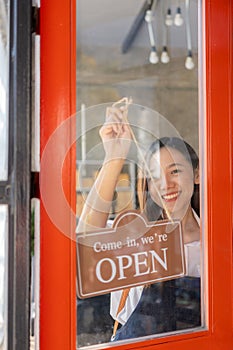 Happy young business owner standing holding open sign Happy Asian woman wearing