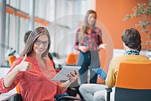 Happy young business woman with her staff, people group in background at modern bright office indoors