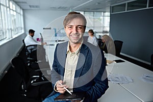 Happy young businessman in businesswear sitting on desk with digital tablet and digitized pen in office