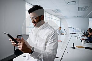 Happy young businessman in businesswear smiling and using digital tablet in office