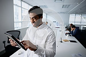 Happy young businessman in businesswear using digital tablet by desk in office photo