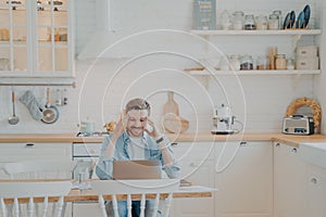 Happy young businessman in casual clothes working with computer at home