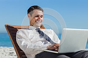 Happy young businessman on a deck chair using his computer