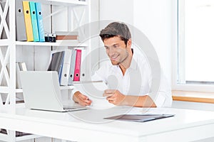 Happy young businessman holding notepad and looking at computer screen