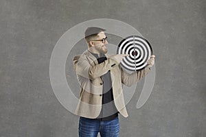 Happy young businessman holding a shooting target and pointing right at the bullseye