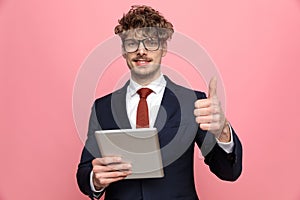 Happy young businessman holding tab and making thumbs up sign