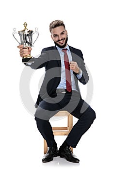 Happy young businessman holding trophy and smiling