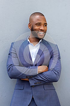 Happy young businessman leaning against wall with his arms crossed