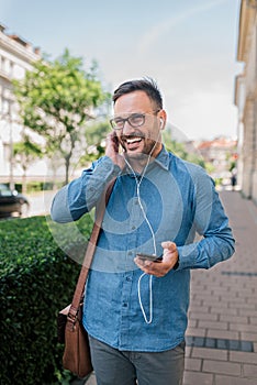 Happy young businessman listening music through headphones on cellphone at the city