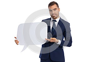 Happy young businessman in navy blue suit presenting speech bubble