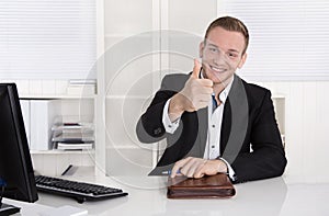 Happy young businessman sitting in his office making thumb up ge