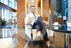 Happy young businessman sitting on sofa in hotel lobby