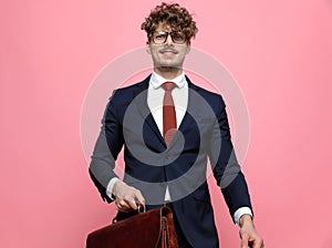 Happy young businessman in suit holding suitcase and smiling