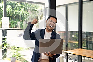 Happy young businessman in suit looking at laptop excited by good news online, lucky successful winner man standing at