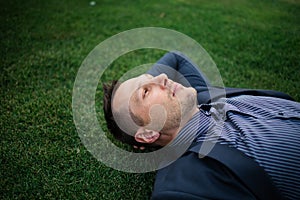 Happy Young businessman in a suit lying on the green grass and relaxing in park.