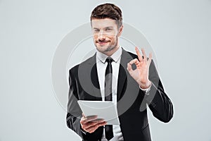 Happy young businessman with tablet winking and showing ok sign