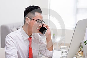 Happy young businessman talking on cell phone and using computer