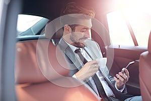 Happy young businessman using mobile phone in back seat of car