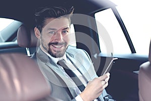 Happy young businessman using mobile phone in back seat of car