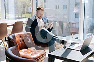 Happy young businessman wearing fashion suit is using mobile phone in modern office room