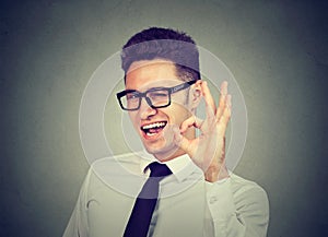 Happy young businessman winking and showing ok sign