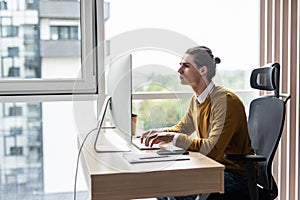 happy young businessman working on desktop computer at his desk in modern bright startup office interior