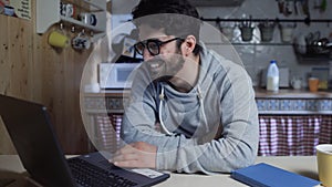 Happy young businessman working on laptop in kitchen at home at night