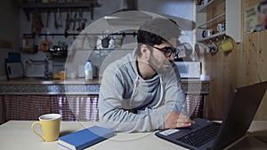 Happy young businessman working on laptop in kitchen at home at night