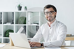 happy young businessman working with laptop at modern office and looking