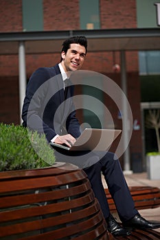 Happy young businessman working outdoors with laptop