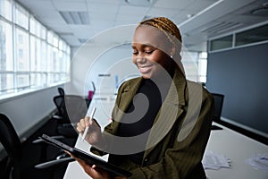 Happy young businesswoman in businesswear using digital tablet and digitized pen by desk in office photo