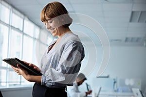 Happy young businesswoman in businesswear working on digital tablet in corporate office