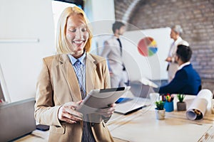 Young businesswoman holding digital tablet with team discussing project in the background