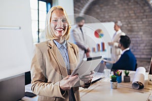 Young businesswoman holding digital tablet with team discussing project in the background