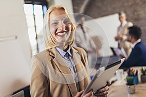 Young businesswoman holding digital tablet with team discussing project in the background