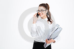 Happy young businesswoman holding folders and talking on mobile phone