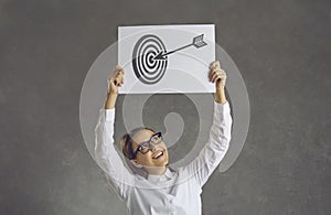 Happy young businesswoman holding picture of arrow in bullseye of shooting target