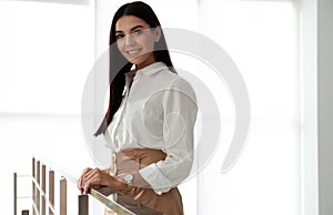 Happy young businesswoman leaning on railing in office