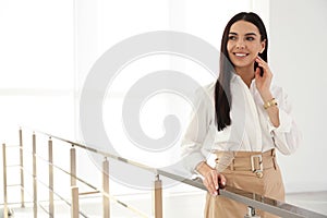 Happy young businesswoman leaning on railing in office. Space for text