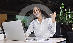 Happy young businesswoman looking at laptop computer in office, Excited african american woman working at her workplace